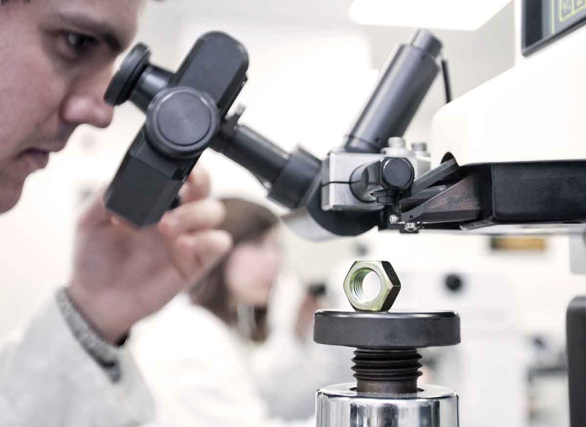 Engineer analyzing a metal nut through a microscope